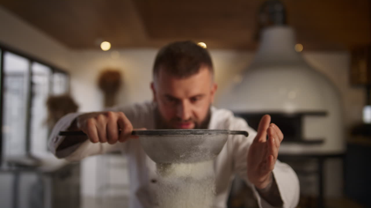 Baker man sifting flour using sieve in culinary restaurant. Chef cooking in cafe