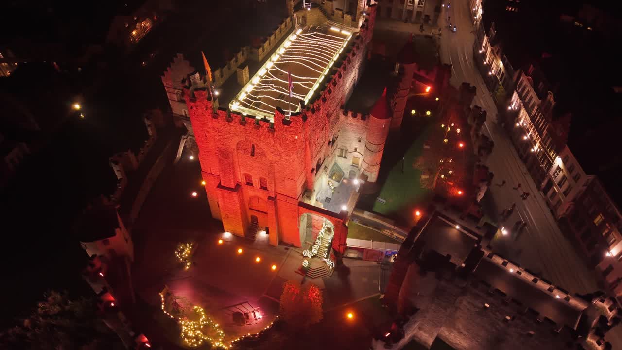 Ripresa aerea del Castello Gravensteen illuminato a Gand, che ne mette in risalto l'architettura medievale e la sua presenza imponente all'interno della città di notte.