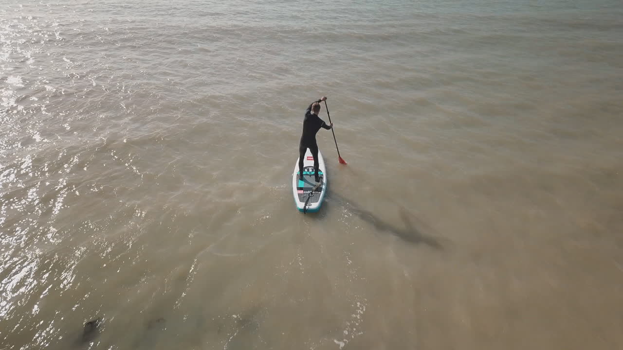 joven salta a la tabla de remo en el mar con un bote, agua brillante y cielo azul en el fondo