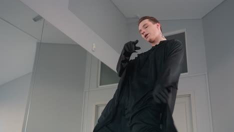 young dancer in flowing black costume leans back with arm extended overhead, performing intense expressive move in mirrored studio under soft natural light