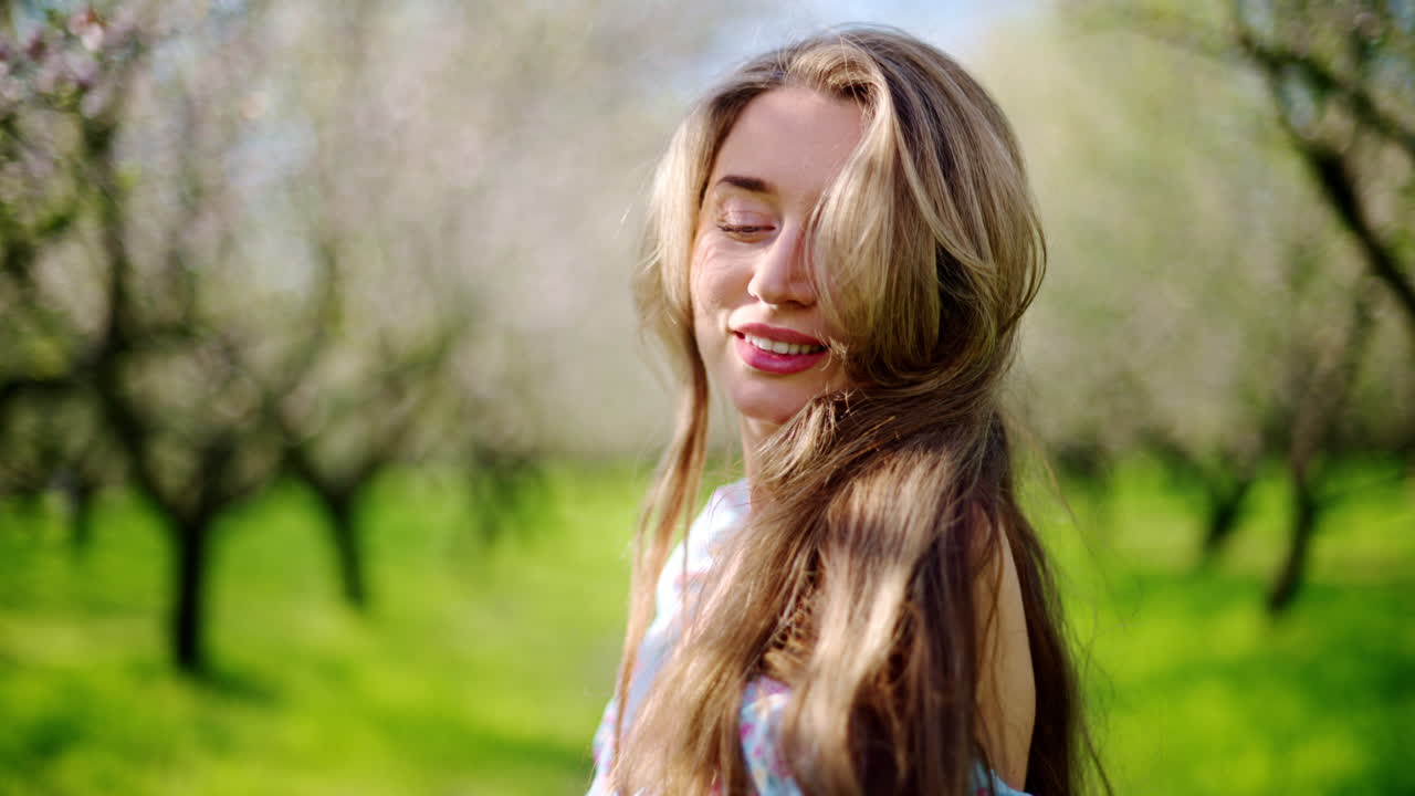 Brunette woman in a blue dress enjoying a field of blooming almond trees