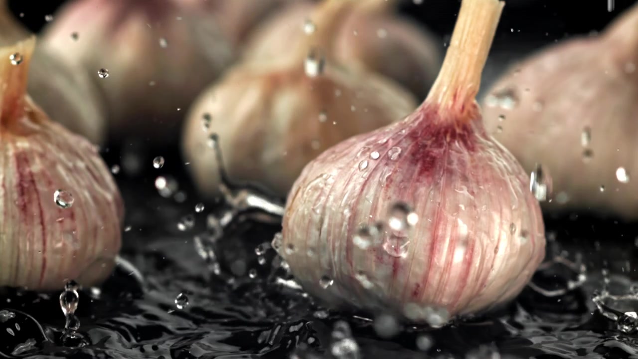 Bulbi d'aglio freschi che schizzano nell'acqua al rallentatore.