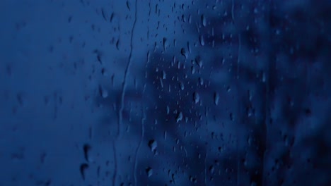 Regnerische-Sturmtröpfchen-In-Der-Nacht,-Launisches-Wetter-Fallen-Fensterglas-Nahaufnahme-Bokeh-Herunter