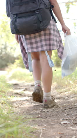 vertical video: hiking on trail, woman with backpack and plastic bag, enjoying nature