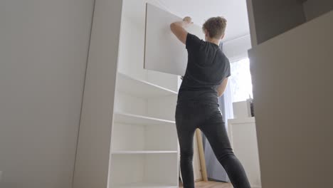 young person install shelves into new modern closet, back view