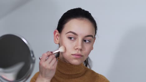 woman applying foundation or blusher on her face lookin in circle mirror