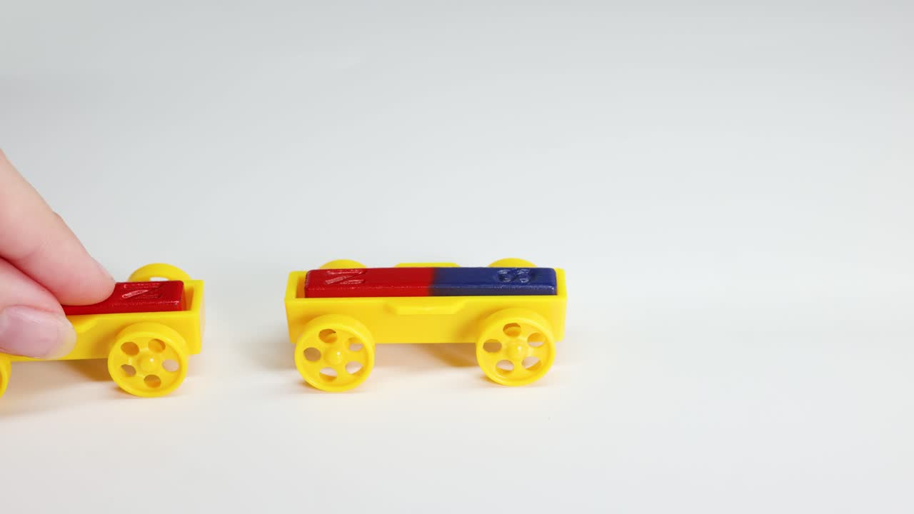 Hands manipulate colorful toy cars to illustrate magnetic attraction and repulsion on a white background with bright lighting