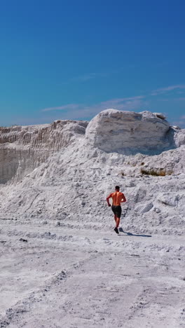Aerial view on white canyon and a sportsman outdoors. Young athlete walking on beautiful white hill on the natural background in summer. Shirtless athlete in shorts under blue sky. Vertical video
