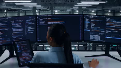 Back View Of Asian Woman Developer Working With Tablet While Write Code With Multiple Computer Screens In Data Center