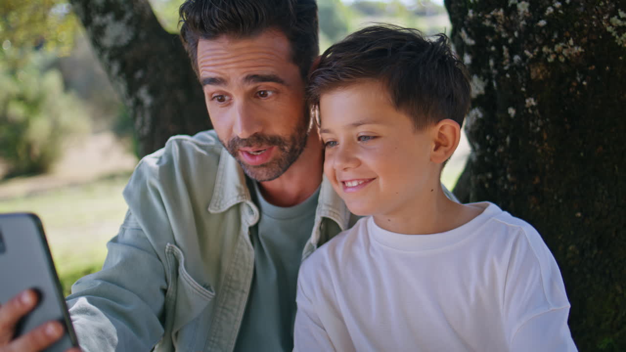 Father kid talking smartphone at summer forest closeup. Smiling family calling