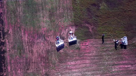 Top-down-rotating-aerial-shot-pull-up-to-reveal-cranberry-field-workers-moving-through-the-bog-on-harvesting-machines