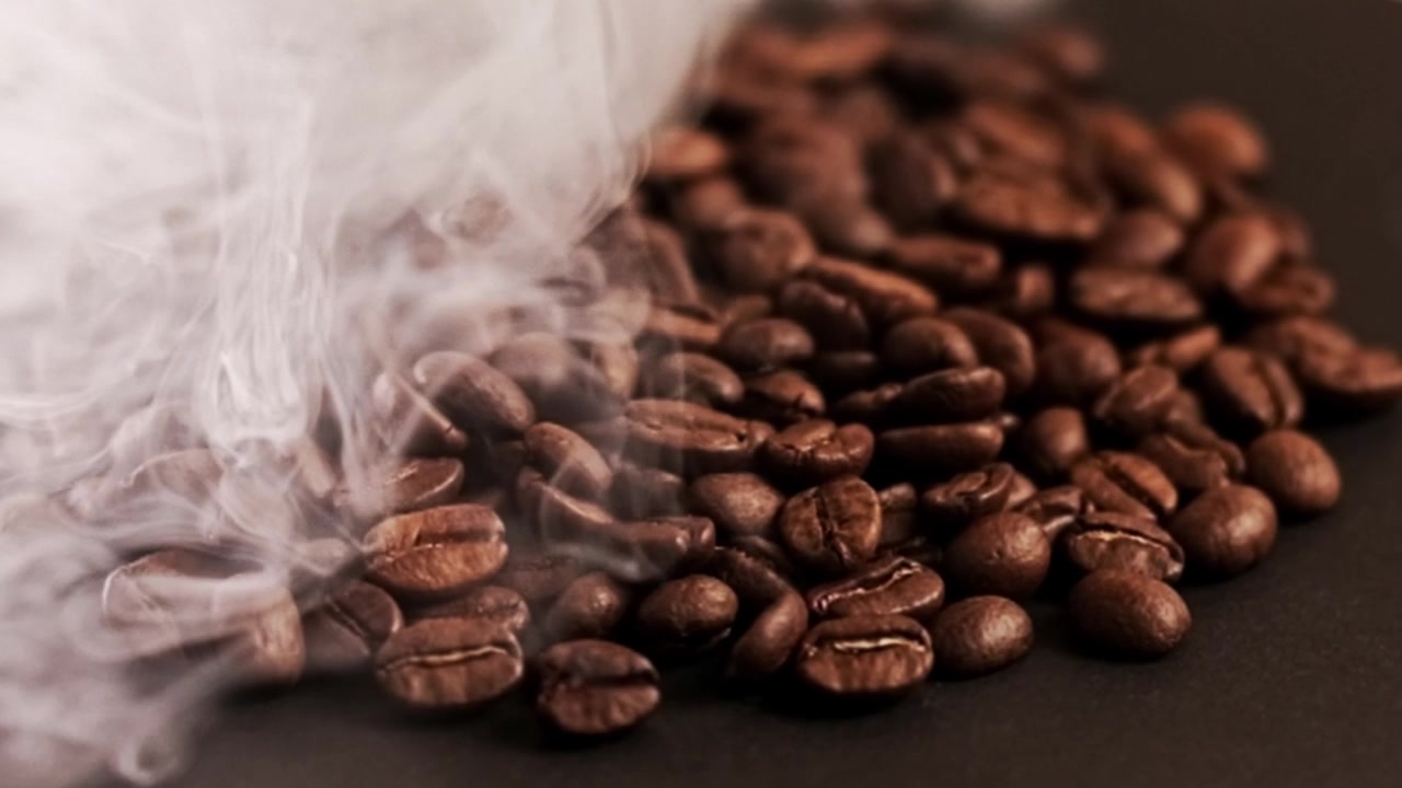 Detalles de granos de café calientes y ahumados girando sobre una superficie negra.