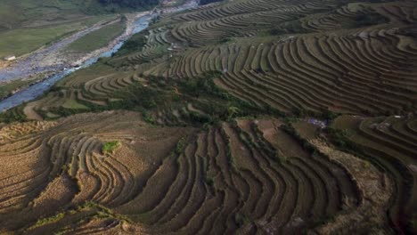 Aerial-view-over-amazing-rice-terraced-green-misty-mountains-and-river-in-Sapa,-Vietnam-at-dusk-as-sun-sets