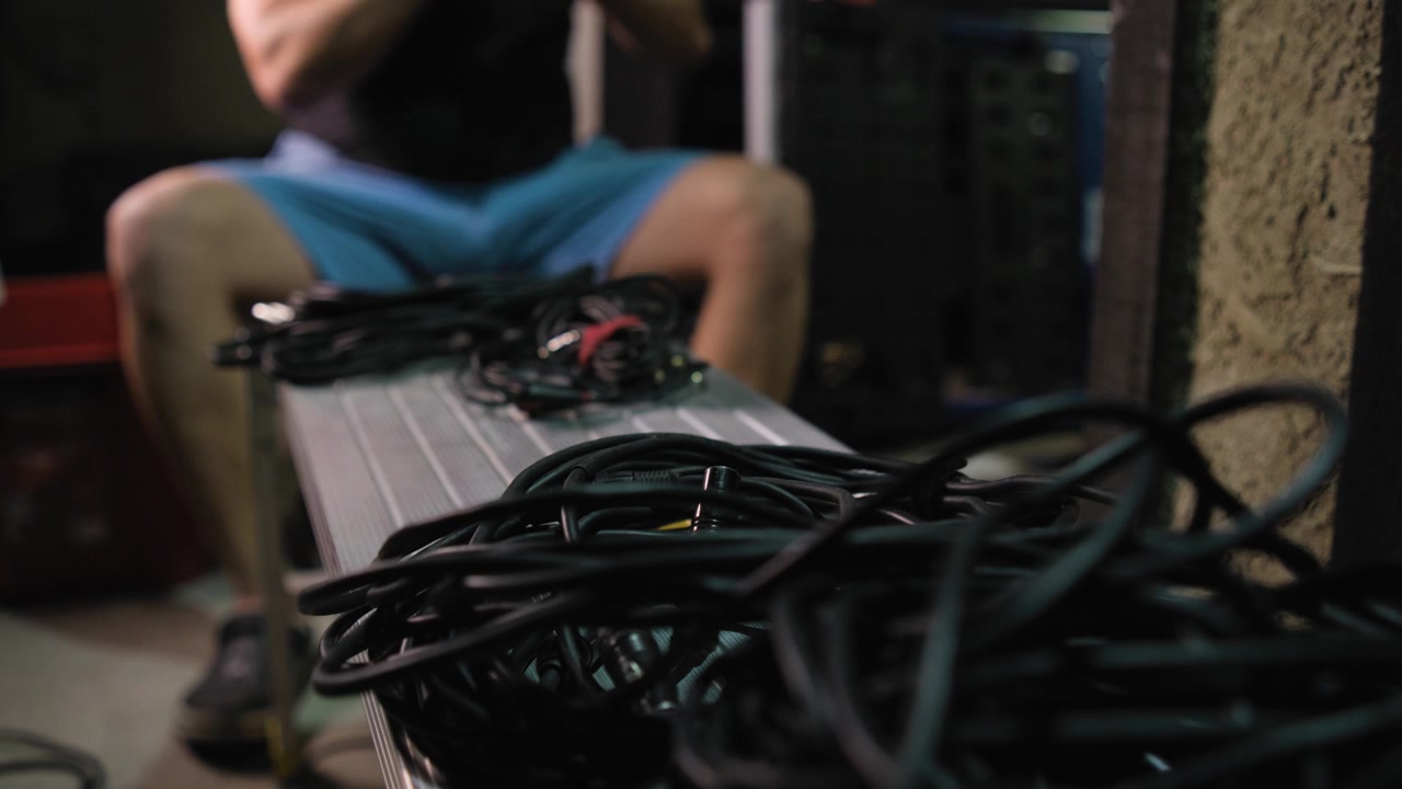 Close view of audio cables with a young man organizing event equipment in the background near a garage.