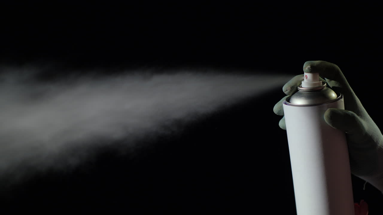 la mano con una lata de aerosol la rocía sobre un fondo negro