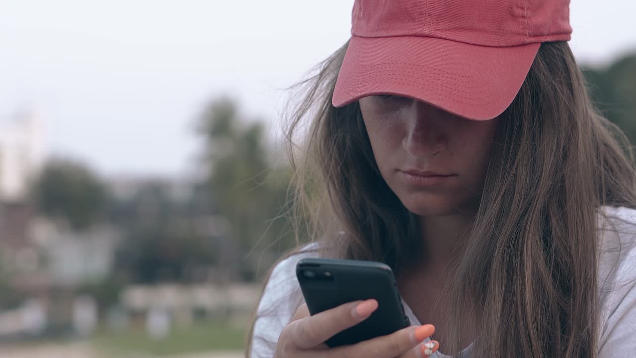 chica con cabello largo y oscuro en gorra roja navega por internet en el teléfono