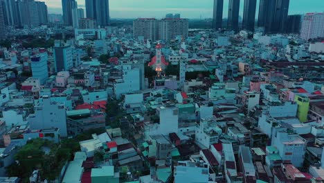 Early-morning-drone-fly-in-over-modern-urban-rooftops-away-from-illuminated-French-colonial-Catholic-Church-with-massive-buildings-in-Silhouette