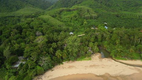 Aerial-tilt-up-shot-of-tropical-forest-hills-with-sandy-beach-and-river-on-Koh-Lanta-in-Thailand