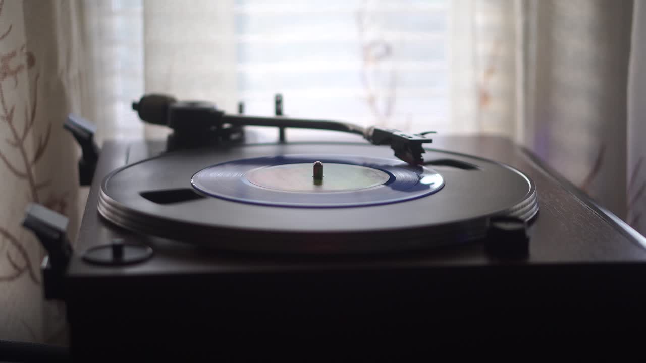 Avvio della riproduzione di un disco in vinile singolo blu vicino a una finestra e una tenda in un salotto
