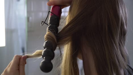 chica de pelo rubio rizándose el pelo, preparándose para la noche