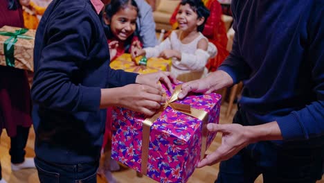 multigenerational family members joyfully exchanging wrapped presents during warm, festive holiday gathering inside elegantly decorated living room with cheerful atmosphere