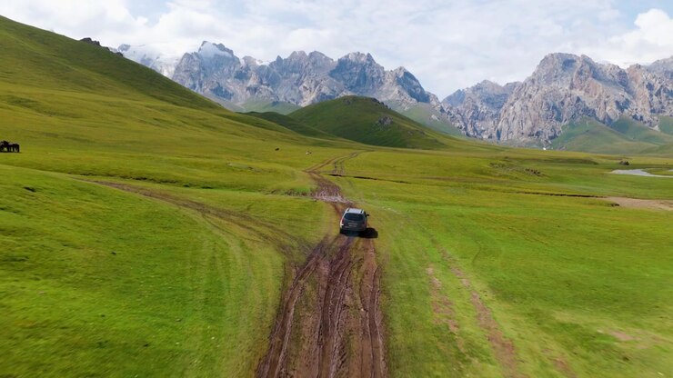 Veicolo fuoristrada che guida su una strada fangosa attraverso le colline verdi negli altopiani del Kirghizistan. - Ripresa aerea in allontanamento