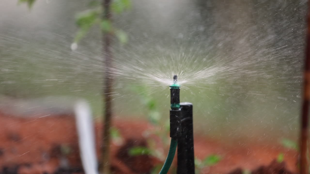 Primo piano di un impianto di irrigazione che spruzza acqua sull'agricoltura con bokeh.