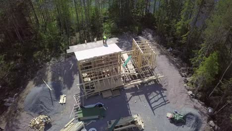 sitio de construcción de una pequeña casa de campo con una hermosa orilla del río, constructor con pistola de clavos trabajando en el techo, antena 4k