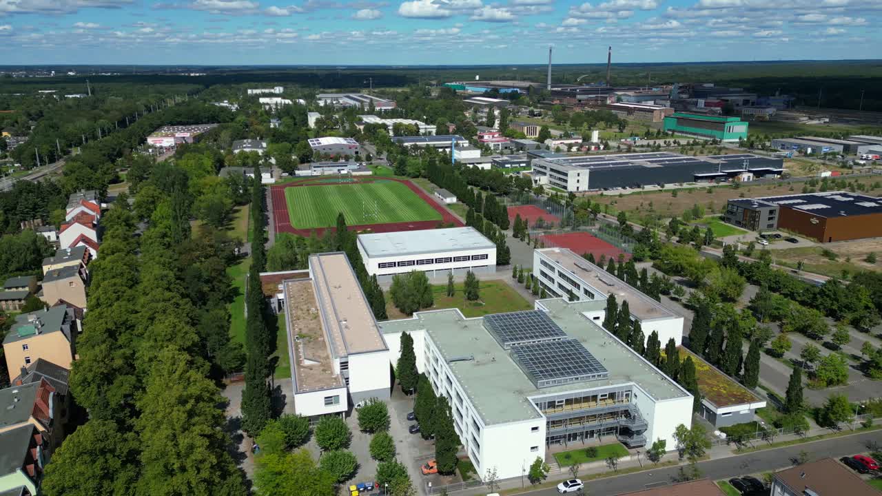 Hennigsdorf High School showcasing its modern architecture, sports facilities, parking area, surrounding urban landscape. Majestic aerial view flight wide orbit overview drone