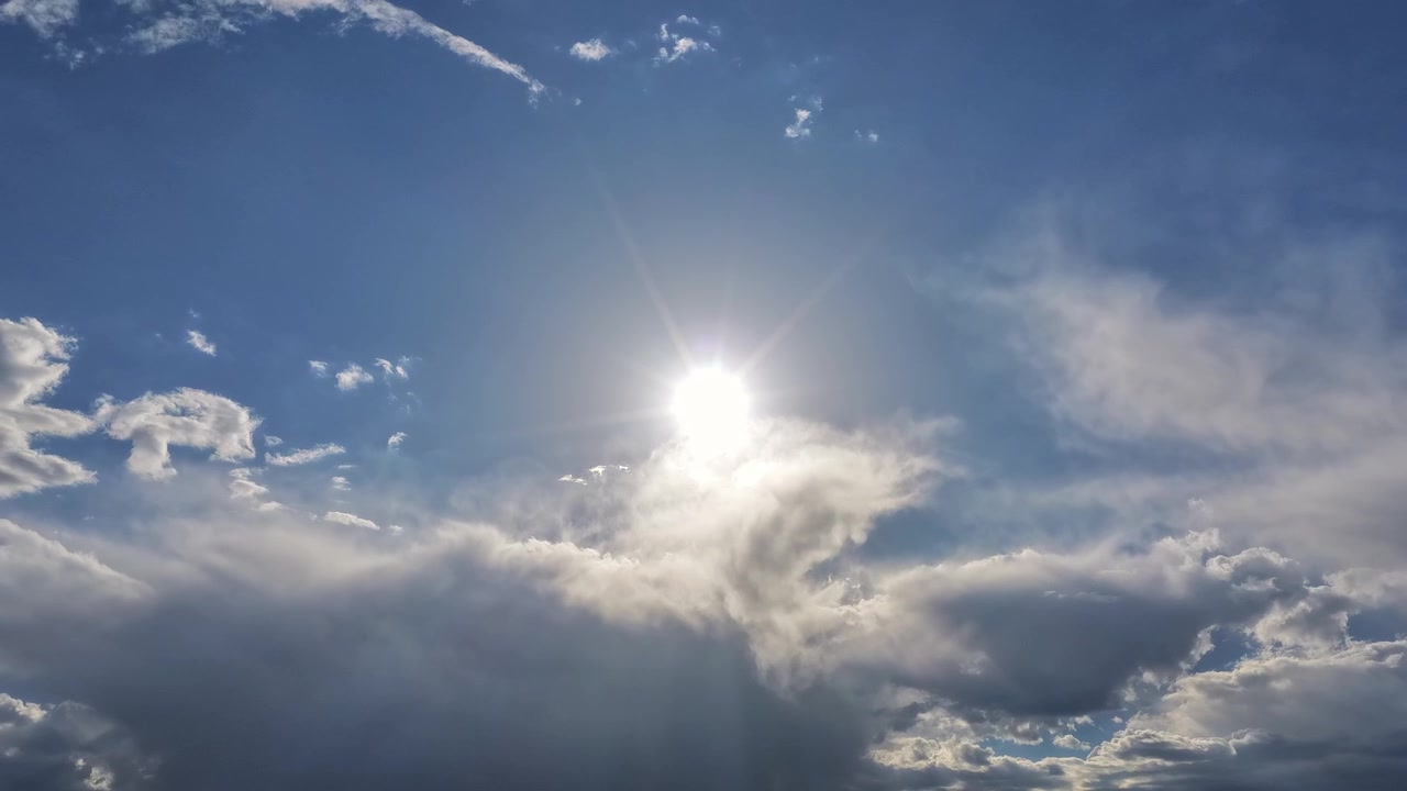 4K UHD stabil timelapse fokuseret direkte på en strålende sol med et stjerneglimt. Bløde, tågede skylag bevæger sig opad hen over den klare blå himmel og dækker til sidst lyset.