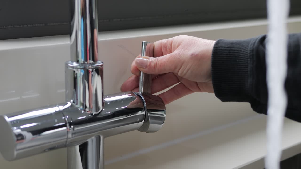 Turning on a kitchen tap, slow motion close-up of stainless steel faucet and lever