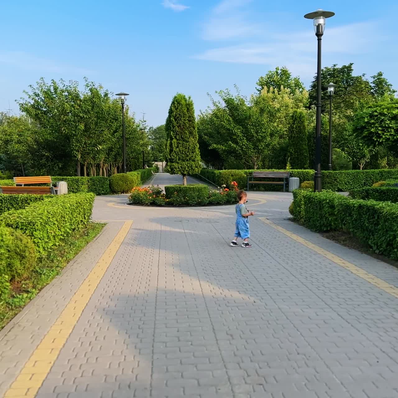 Little baby boy wearing jeans romper is in the green park. Active toddler runs by the road and stops