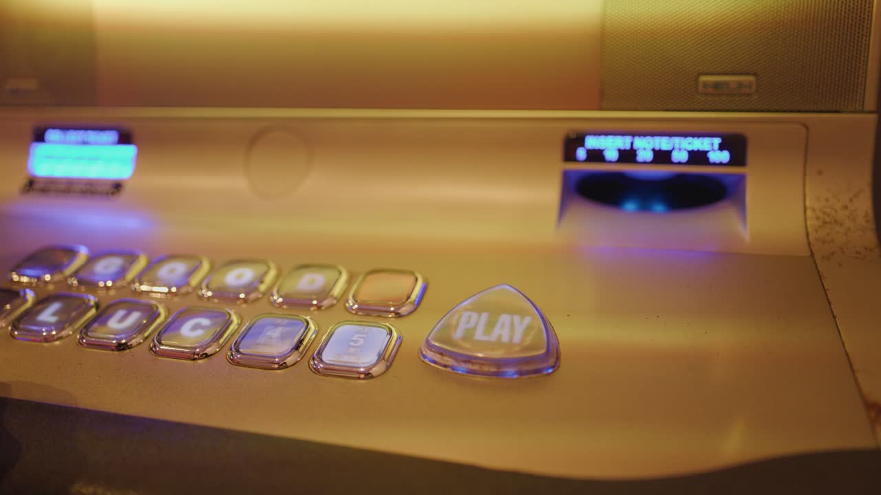 Primo piano della console illuminata di una slot machine mentre una mano preme il pulsante di riproduzione sotto una luce calda
