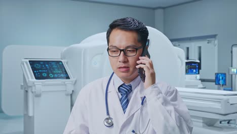 Close Up Of Asian Male Doctor Shouting On Smartphone While Standing With MRI Machine In The Hospital