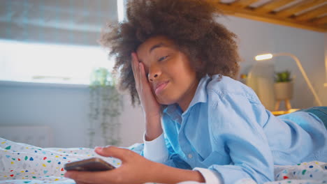 Tired-Or-Worried-Boy-In-Bedroom-Lying-On-Bed-Holding-Mobile-Phone-Being-Bullied-Online