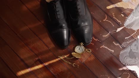 leather shoes and gold pocket watch near lace curtains on hardwood floor