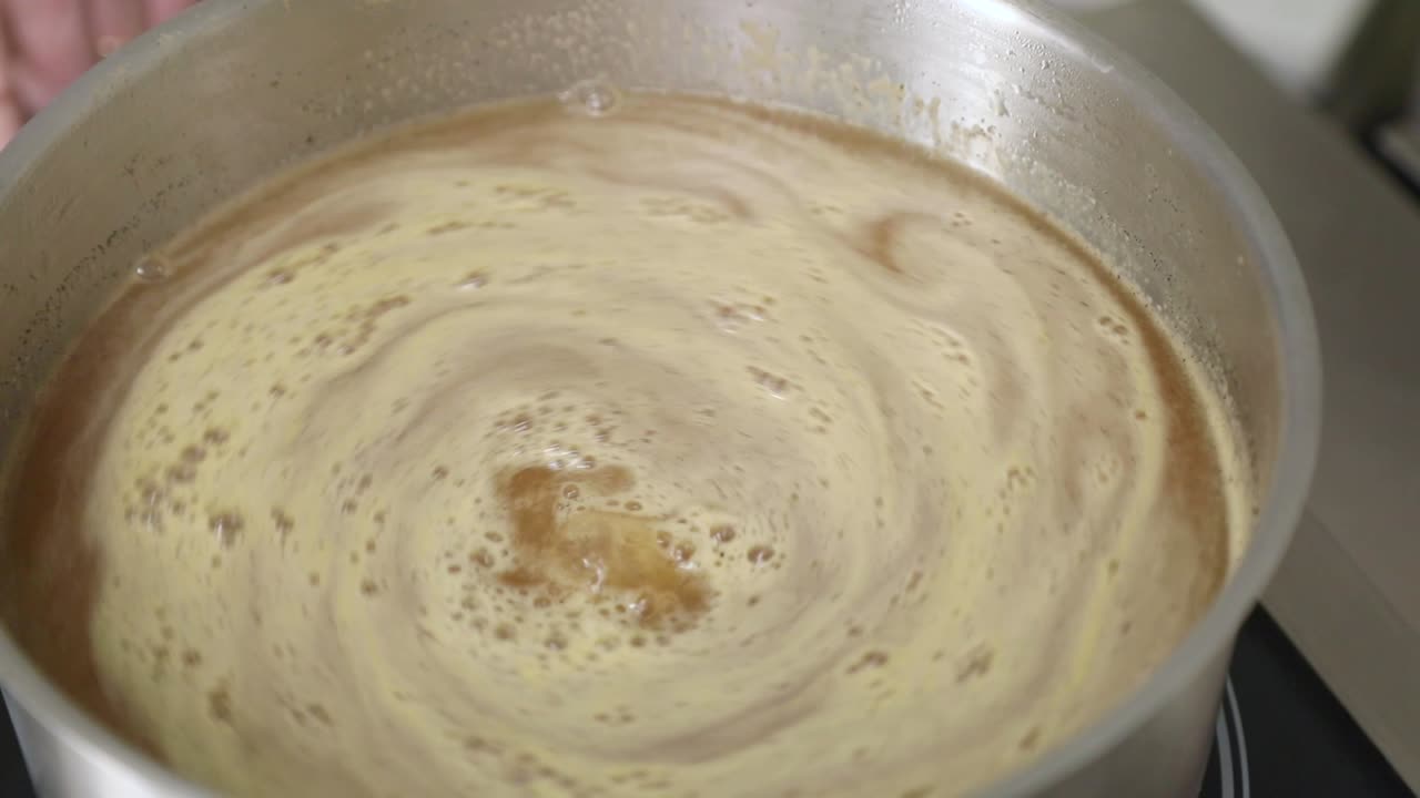 Cucinare e mescolare marmellata di mele in una pentola con una frusta - primo piano, slow motion.