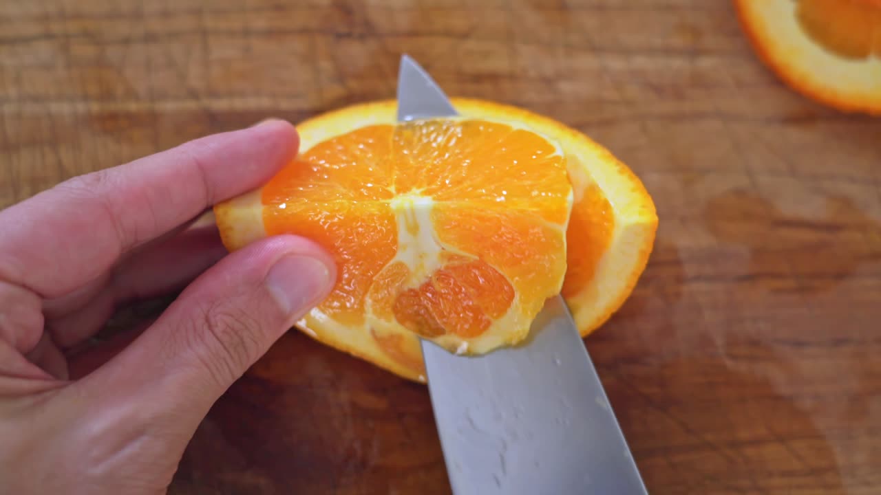la mano caucásica pela la naranja con un cuchillo grande de plata en una tabla de cortar de madera