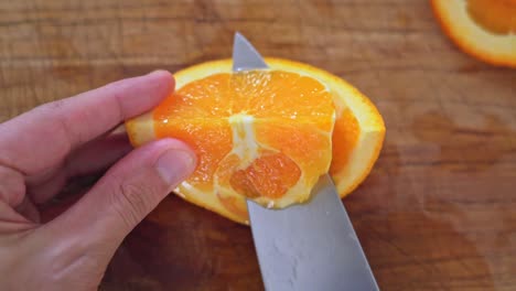 caucasian hand peels orange with a big silver knife on a wooden cutting board