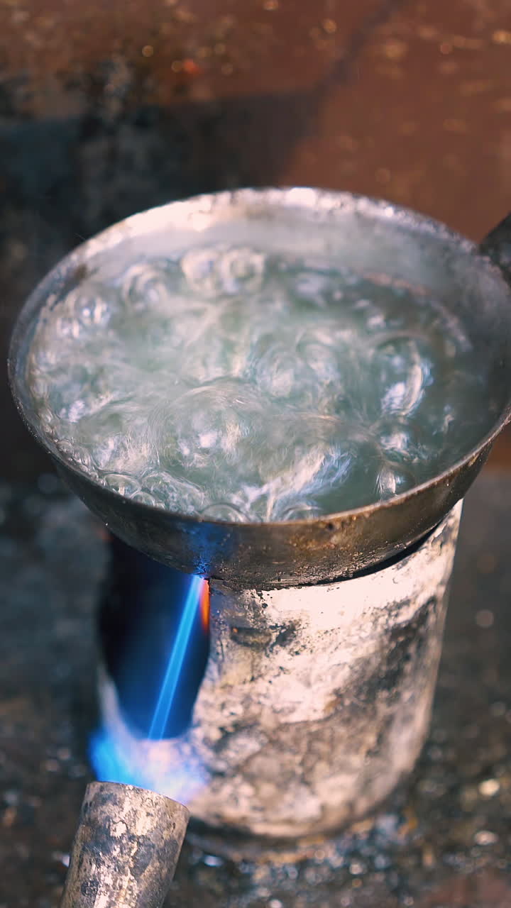 CU: skilled goldsmith processes beautiful gold chain in boiling liquid on gas burner at traditional workplace close view