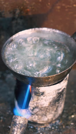 cu: skilled goldsmith processes beautiful gold chain in boiling liquid on gas burner at traditional workplace close view