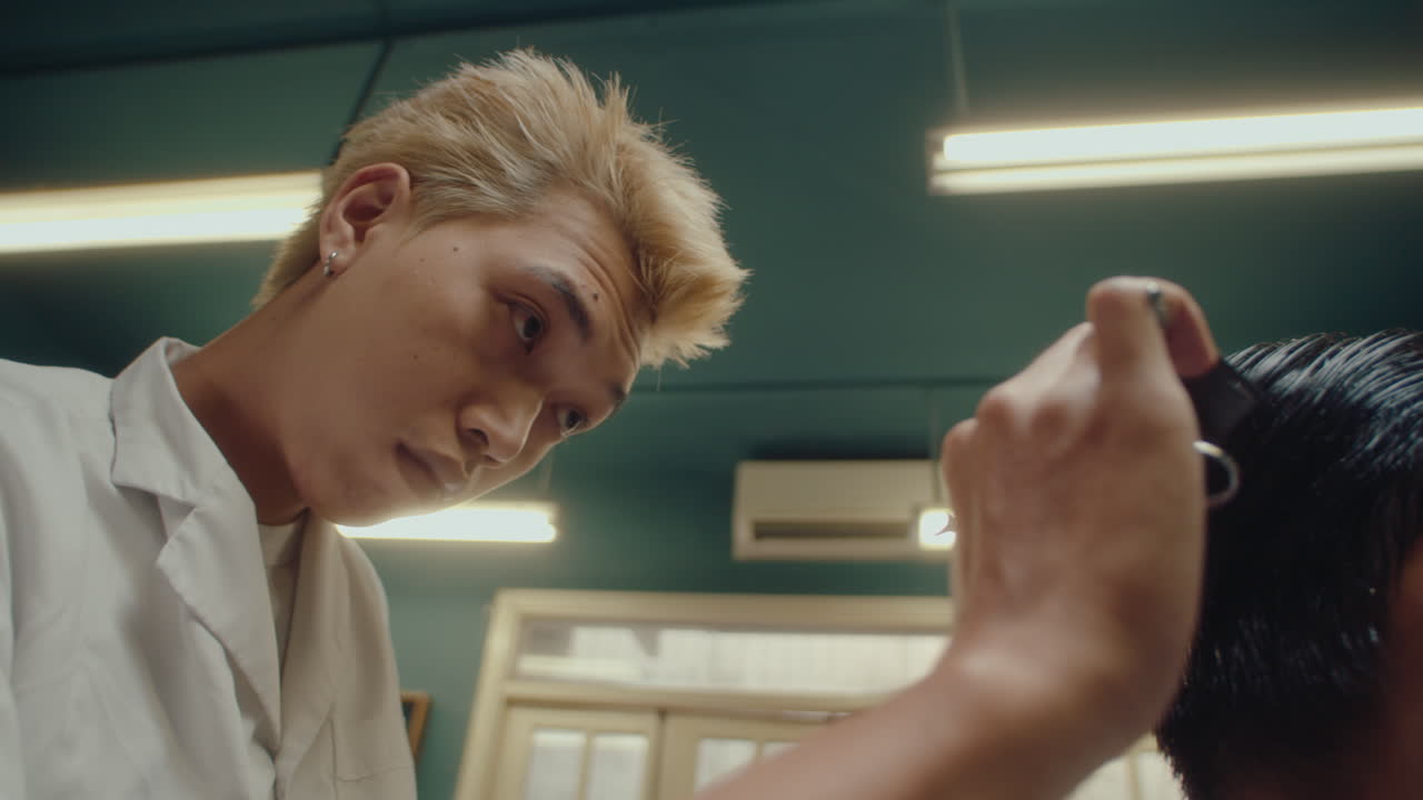 Asian Hairdresser Giving a Haircut to Client in Barbershop