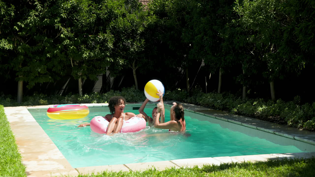 Diverse female friends enjoying pool time with colorful inflatables, laughing and playing together