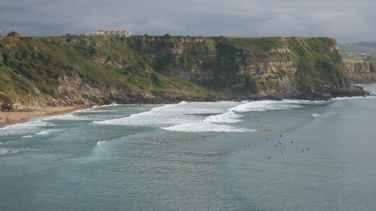 Surfers ride waves at Los Locos Beach with Punta Sopico cliff and Punta Ballota behind