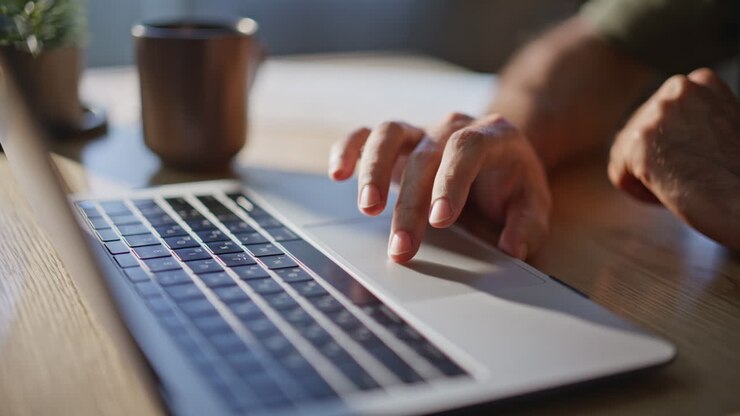 Mani maschili che utilizzano il touchpad in un ufficio illuminato dalla luce solare. Persona che lavora al laptop in ufficio
