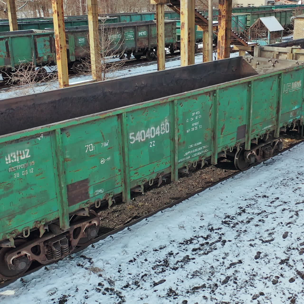 Empty containers are moving slowly on rails on the background of the cargo railway station under bridge at countryside. Aerial view.