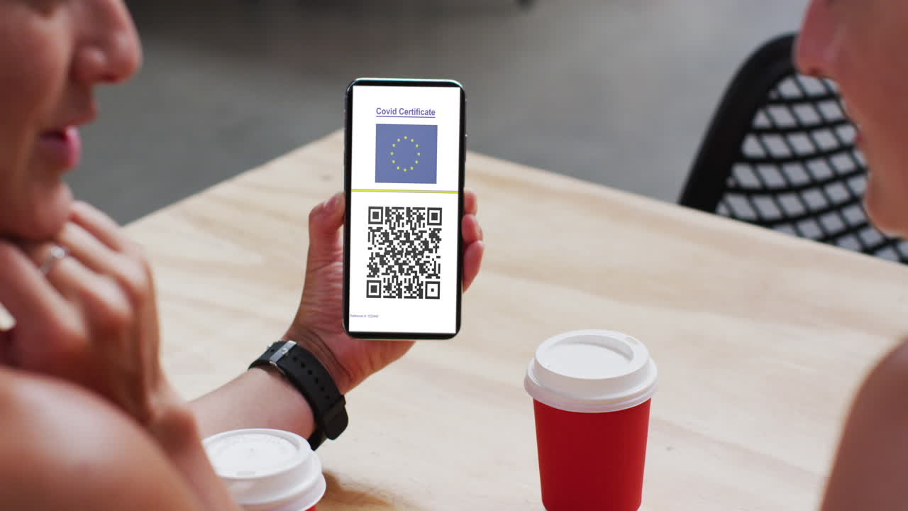 Man at cafe showing smartphone with covid vaccination certificate, eu flag and qr code on screen