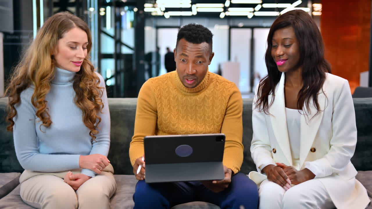 Multiracial group of people in an office discussing business using a tablet while sitting on a sofa