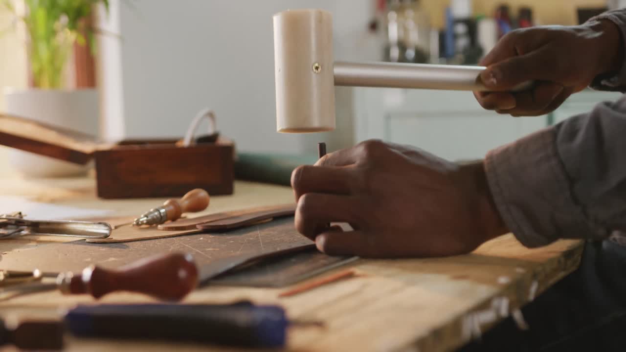 Hands of african american craftsman using tools to make a hole in leather workshop