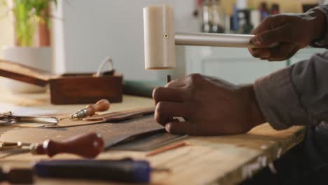 hands of african american craftsman using tools to make a hole in leather workshop